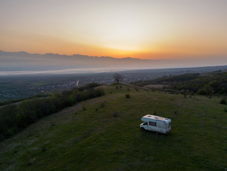 motorhome in a mountain valley, camper on a green meadow at sunrise, aerial shotの写真素材