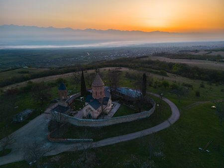 Lonely ancient church in the mountains at dawn between green hills, aerial viewの写真素材