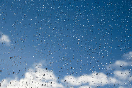 Raindrops on glass on a background of blue sky with clouds