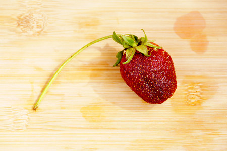 Lonely dark red strawberry on a chopping boardの写真素材