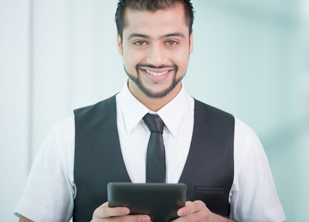Young Asian Indian businessman standing on office background and holding a tablet in handsの写真素材