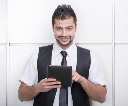 Young Asian Indian businessman standing on office background and holding a tablet in handsの写真素材