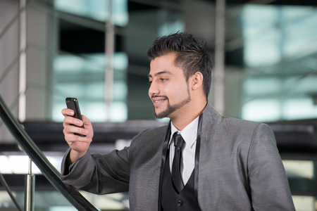 Young Asian Indian businessman standing on office background and talking on the phoneの写真素材