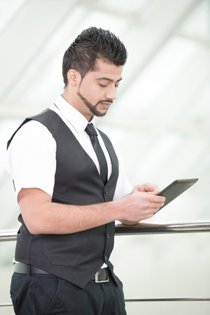 Young Asian Indian businessman standing on office background and holding a tablet in handsの写真素材