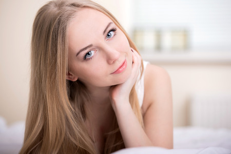 Beautiful young blonde girl lying on a bed in her bedroomの写真素材
