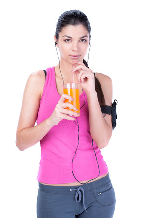 Young beautiful fitness woman drinking juice and listening to music isolated on white の写真素材