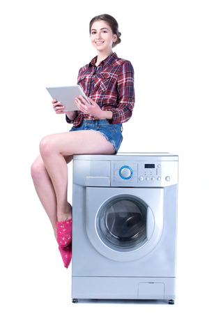 Woman with tablet sitting on the washing machine. Isolated on white の写真素材