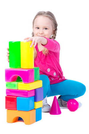 Happy little girl. Child is constructing houses from color toy blocks. Training and development of the imagination. Isolated on white の写真素材