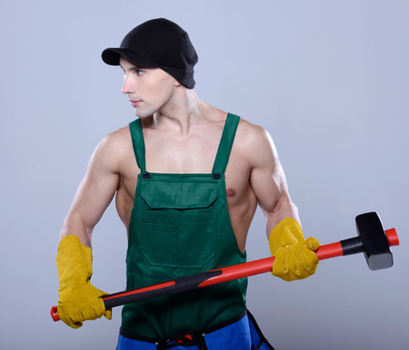 Handsome young topless construction worker with sledge hammer, studio shot, gray backgroundの写真素材