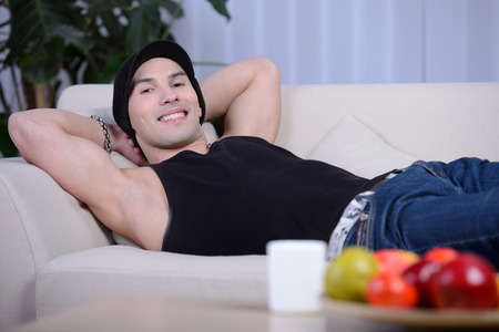 Smiling young man dreaming at his future and relaxing on sofa at homeの写真素材