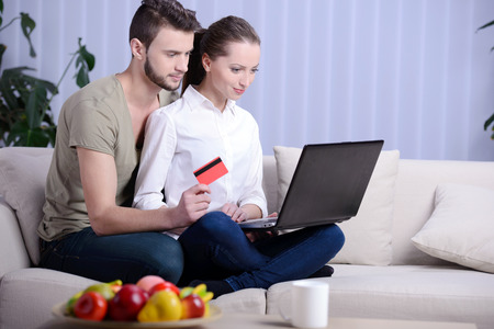 Portrait of happy couple shopping online with credit card in houseの写真素材