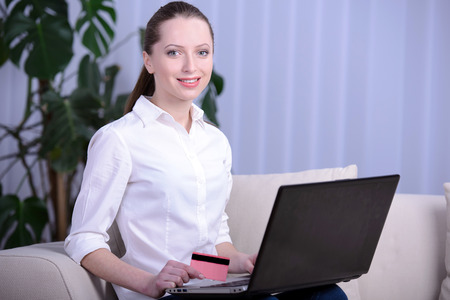 Young girl thinks about purchasing through the internet sitting on the sofaの写真素材
