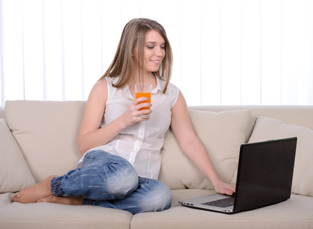 Work at home. Young beautiful woman working with a laptop sitting on sofa at homeの写真素材