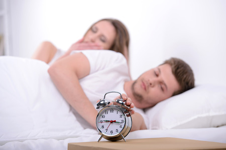 Young couple sleeping together in bed with alarm clockの写真素材