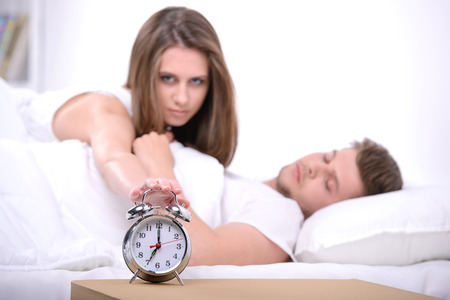 Young couple sleeping together in bed with alarm clockの写真素材