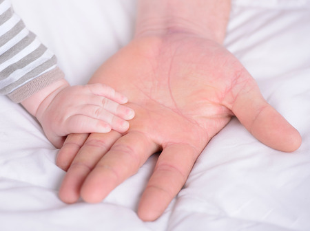 A hand holding a small baby hand of his fatherの写真素材