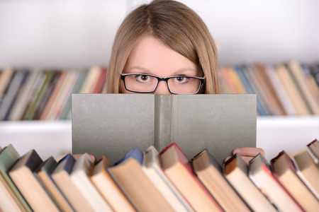 Young student girl with book selection bookshelf, school