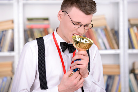 Smart young man intelehent in shirt and tie tie and glasses holding a medal and cup champion standing in the libraryの写真素材