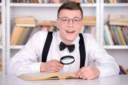 Smart young man intelehent in shirt and tie tie and glasses reading a book on the head while standing in a libraryの写真素材