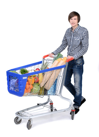 A young male pushing a shopping cart full with groceries isolated on white backgroundの写真素材