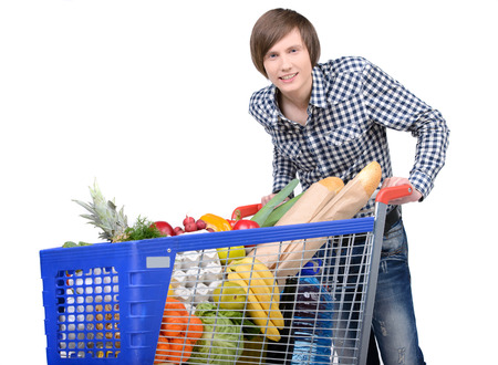 A young male pushing a shopping cart full with groceries isolated on white backgroundの写真素材