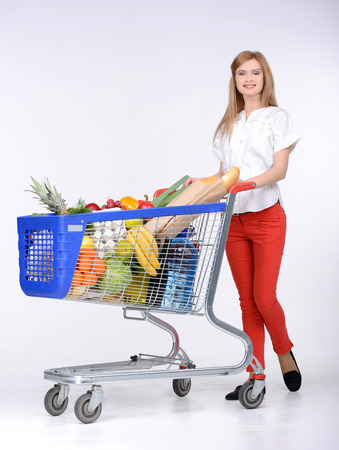 Portrait of a woman holding a shopping basket and shopping cart isolated on white backgroundの写真素材