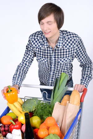 A young male pushing a shopping cart full with groceries isolated on white backgroundの写真素材