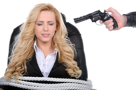 Business woman bound to a chair with rope and aim it to the head with a gun isolated on a white backgroundの写真素材