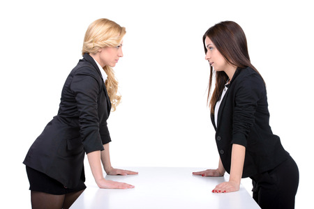 Women confrontation. Two angry women looking at each other while holding their hands on the tableの写真素材
