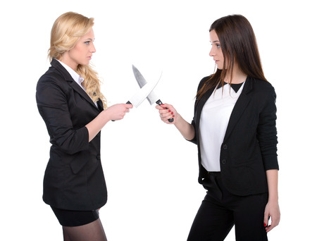 Dishonest partnership. Two young business woman shaking hands and holding knifes.の写真素材