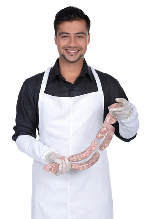 Happy cook holding sausage and smiling. young butcher demonstrating work in handsの写真素材