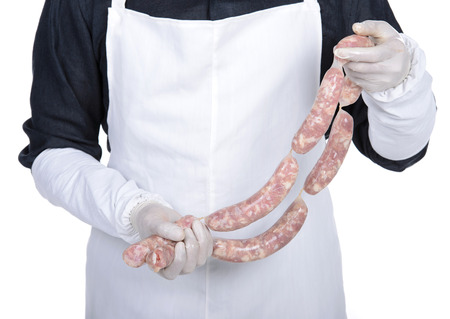 Happy cook holding sausage and smiling. young butcher demonstrating work in handsの写真素材