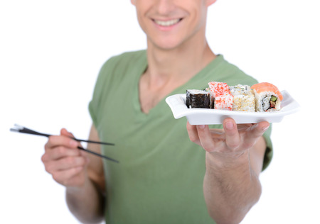 Man eating sushi. Cheerful young man eating sushi while standing isolated on whiteの写真素材