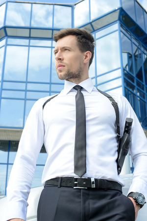 Portrait of a young detective with a gun on a background of the business centerの写真素材