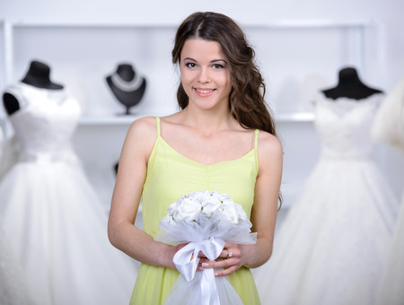 Smiling pretty bride chooses white gown at shop of wedding fashionの写真素材