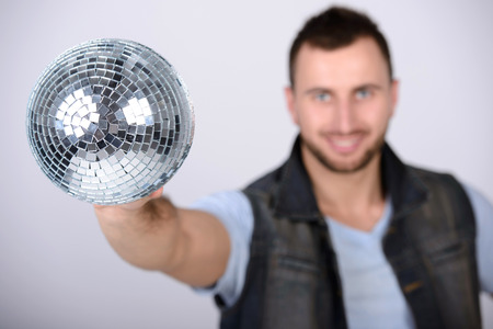 smiling man showing disco shiny ball against dark backgroundの写真素材
