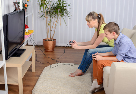 A beautiful woman and her teenage son at home, sitting on a couch playing a video game.の写真素材