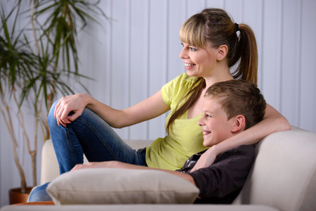 Young mother with her young son watching TV sitting on couch at homeの写真素材