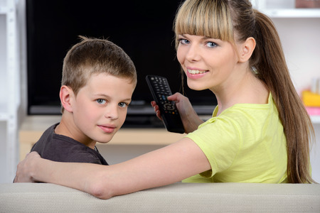 Young mother with her young son watching TV sitting on couch at homeの写真素材