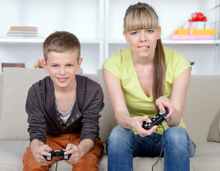 A beautiful woman and her teenage son at home, sitting on a couch playing a video game.の写真素材