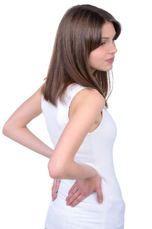 Feeling pain in back. Rear view of young woman holding hands on back and looking away while standing isolated on whiteの写真素材
