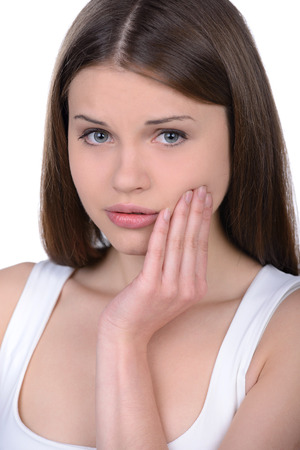 Suffering from toothache. Frustrated young woman touching her cheek and looking at camera while standing isolated on whiteの写真素材