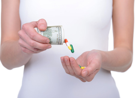 Paid medicine. Cropped image of woman pouring pills from the dollar bills while standing isolated on whiteの写真素材