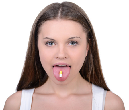 Pill in her mouth. Portrait of young woman holding pill in her mouth and smiling while isolated on whiteの写真素材
