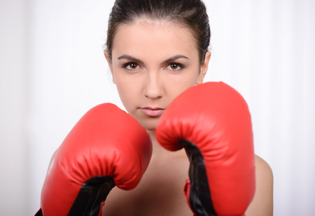 Beautiful young woman training next to a punching bag and wearing boxing glovesの写真素材