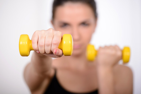 Woman training with dumbbells. Beautiful young woman holding dumbbells and smiling at cameraの写真素材