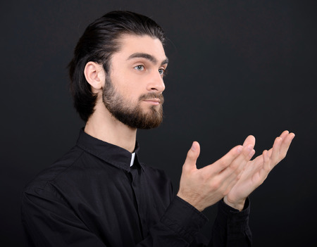 Praying priest. Portrait of priest standing isolated on blackの写真素材
