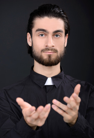 Praying priest. Portrait of priest standing isolated on blackの写真素材