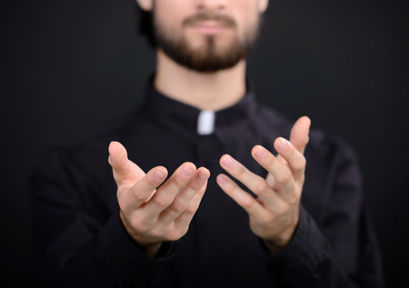 Praying priest. Portrait of priest standing isolated on blackの写真素材