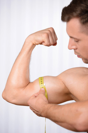 Perfect bicep. Cropped image of muscular man measuring his bicep with measuring tapeの写真素材